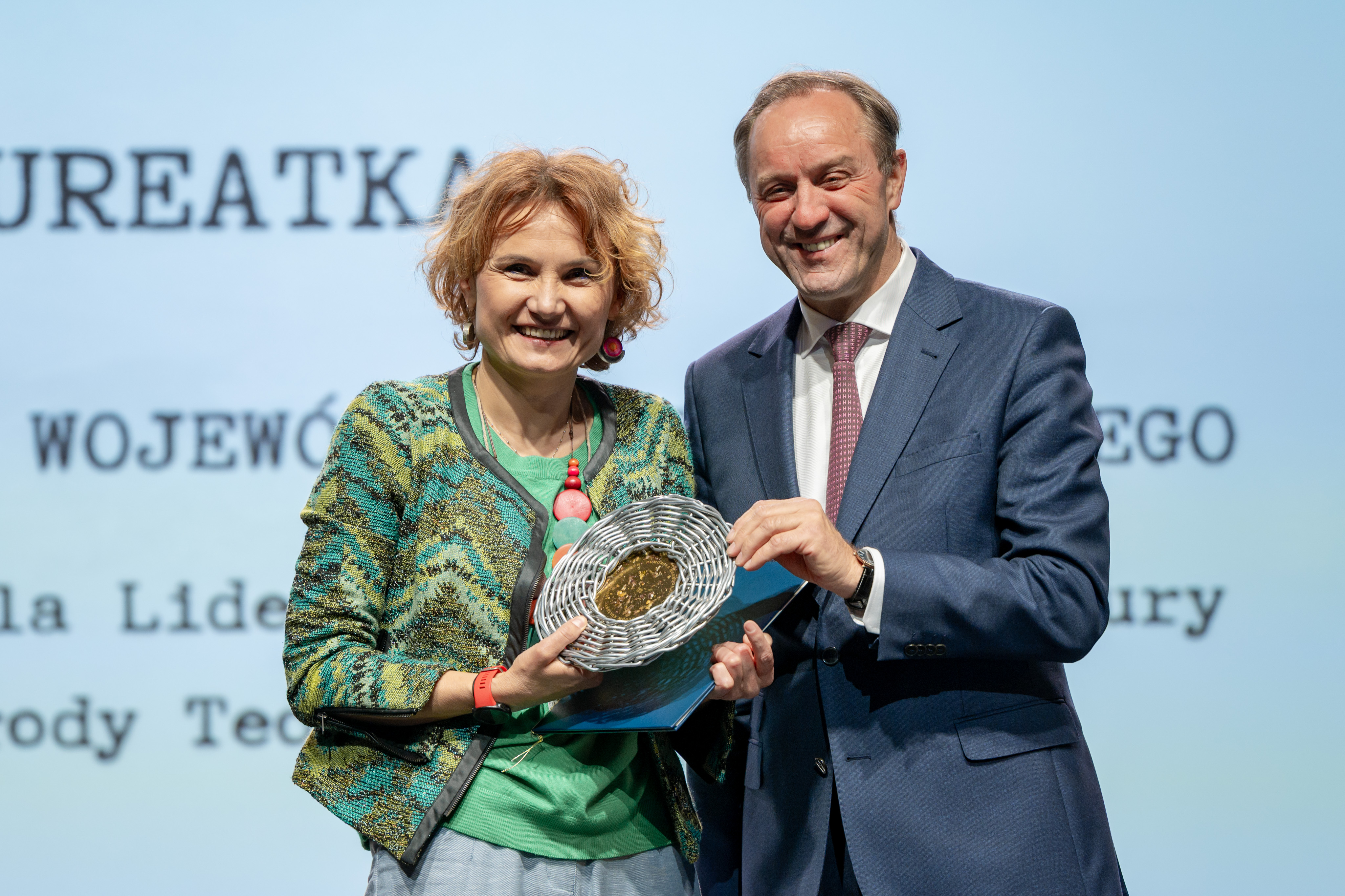 zdjęcie dwóch osób na scenie, trzymają dyplom i stauetkę