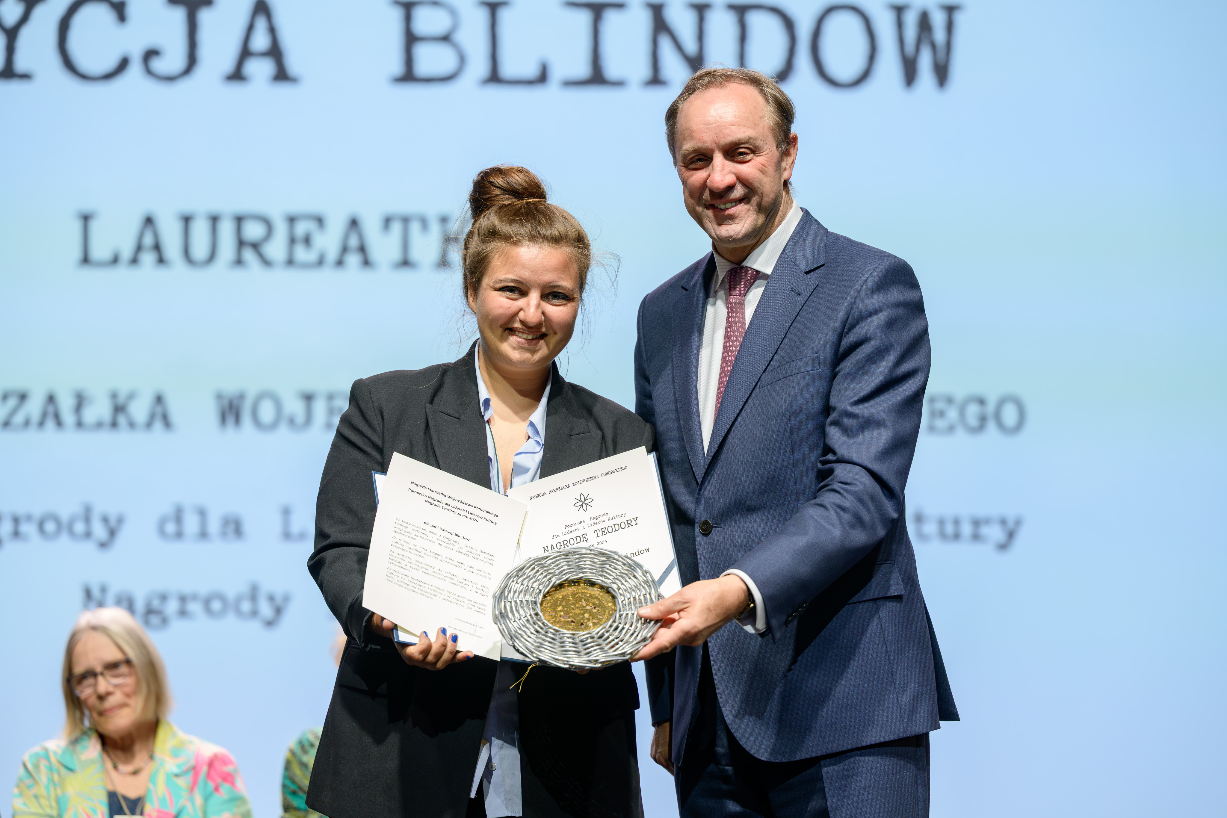 zdjęcie dwóch osób na scenie, trzymają dyplom i stauetkę