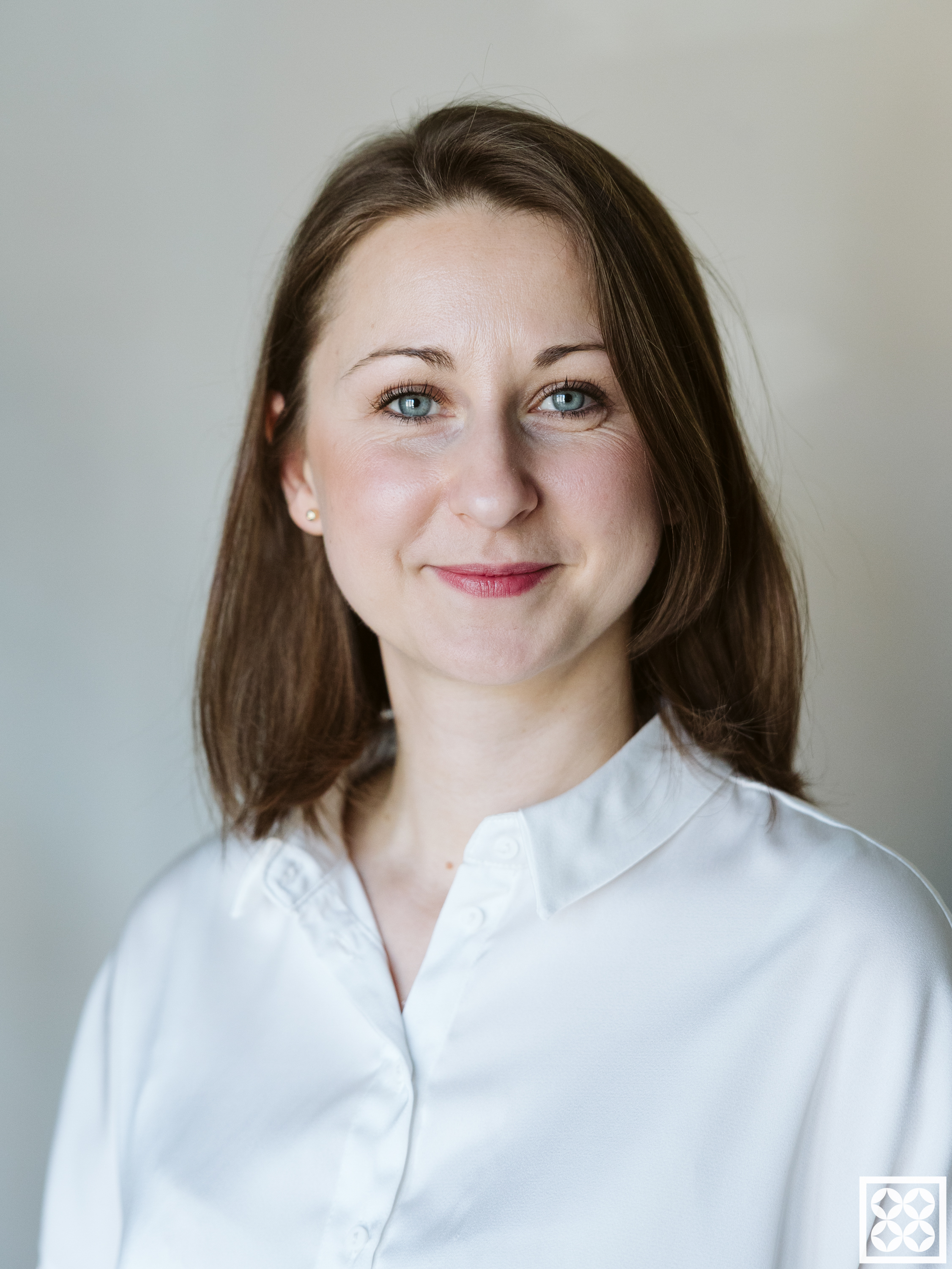 Portret uśmiechniętej kobiety w białej koszuli na jasnym tle.