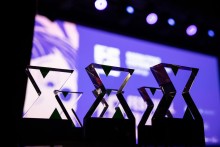 Zbliżenie na kilka statuetek ustawionych na scenie; w tle rozmyte, fioletowo-niebieskie oświetlenie i ekran