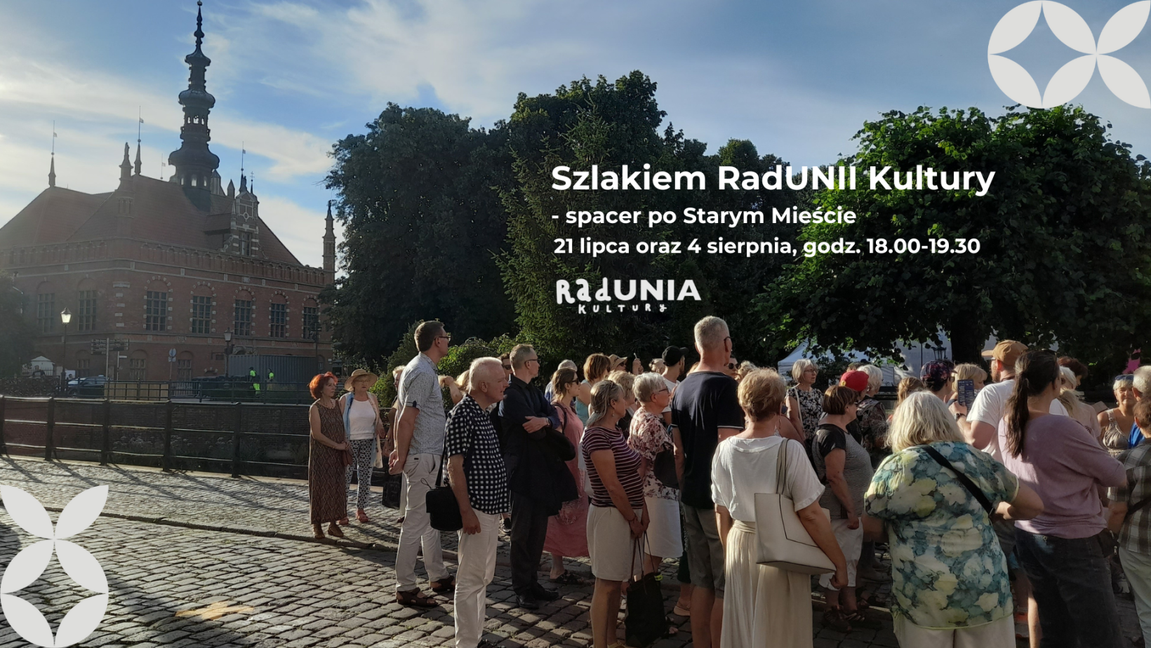 zdjęcie podczas spacaceru, na nim ratusz staromiejski, kilkanaścioro ludzi, napisy z nazwą wydarzenia, godziną, dekoracjami w motywie NCK