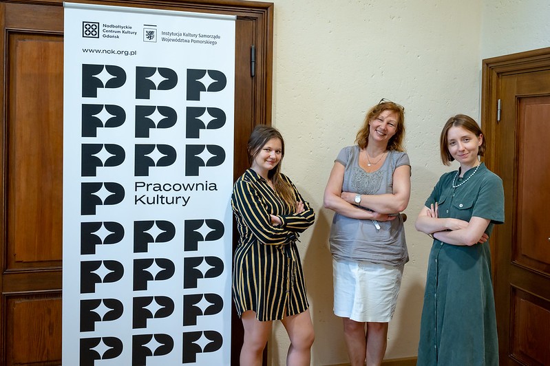 zdjęcie wewnątrz, trzy uśmiechnięte kobiety stoją przy roll-upie NCK
