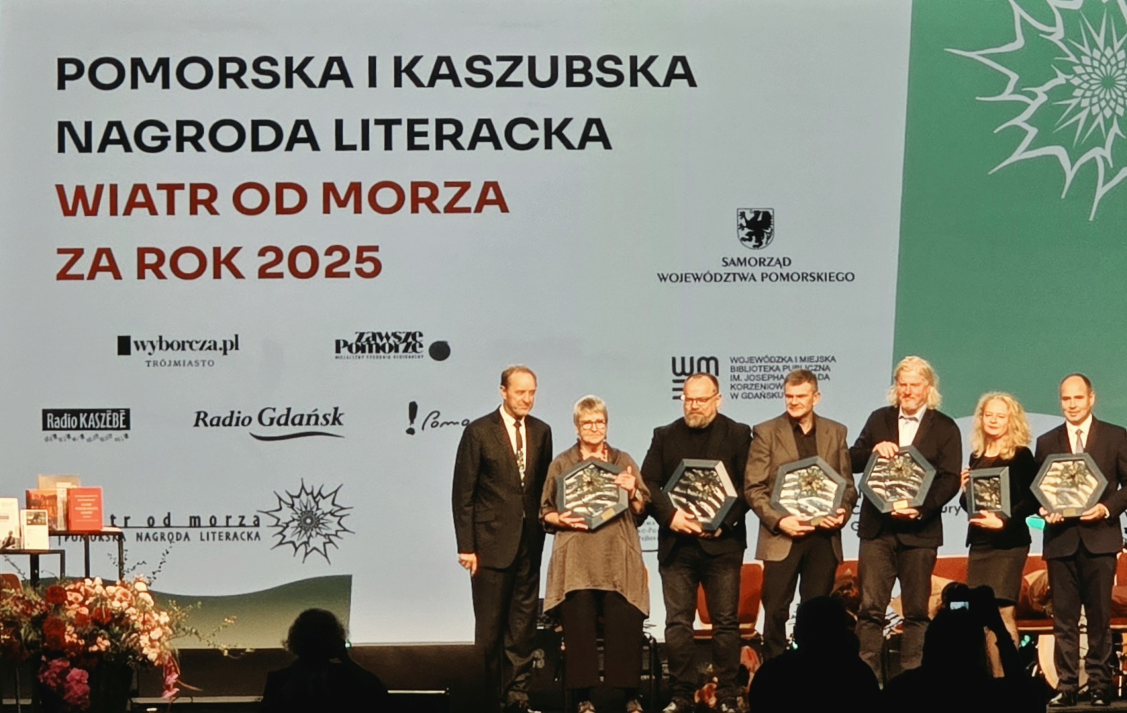 zdjęcie ludzi na scenie, w tle napis "pomorska i kaszubska nagroda literacka "wiatr od morza za rok 2025"