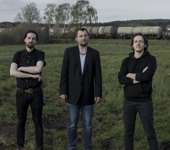 Koncert z cyklu Metropolia Jest Okey w Radiu Gdańsk. Trzech mężczyzn stoi na łące. 30 października 2022. Transmisja wideo i audio.