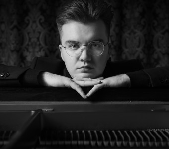 czarno-białe zdjęcie piotra Alexewicza opierającego się o pianino w kwadracie